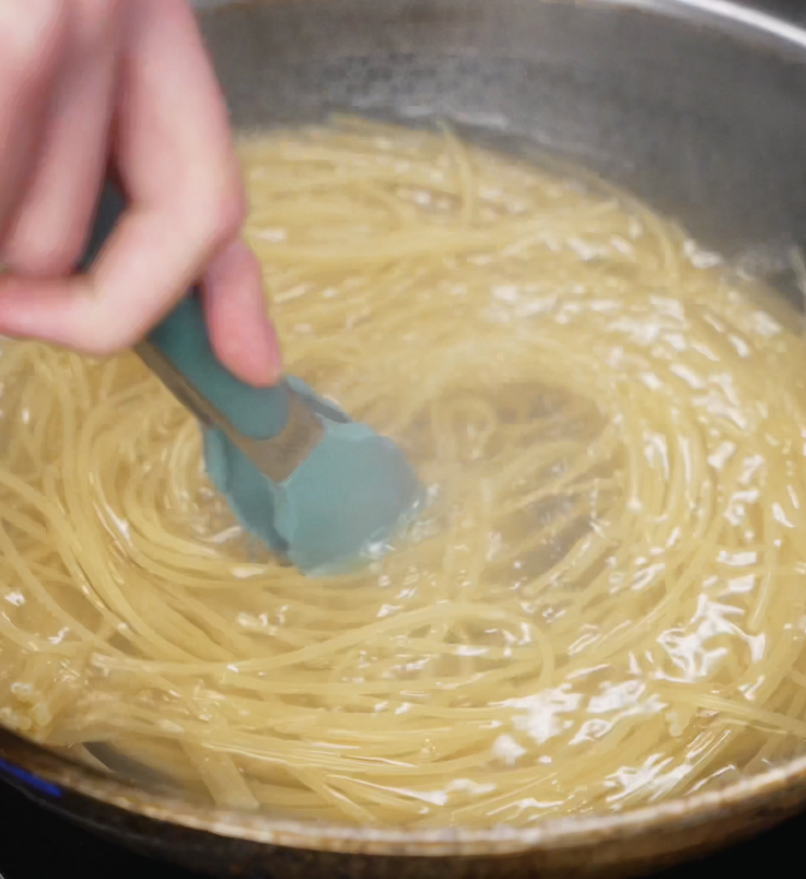 Spaghetti cooking in a pot of salted boiling water, stirred with tongs to ensure even cooking before reaching al dente texture.