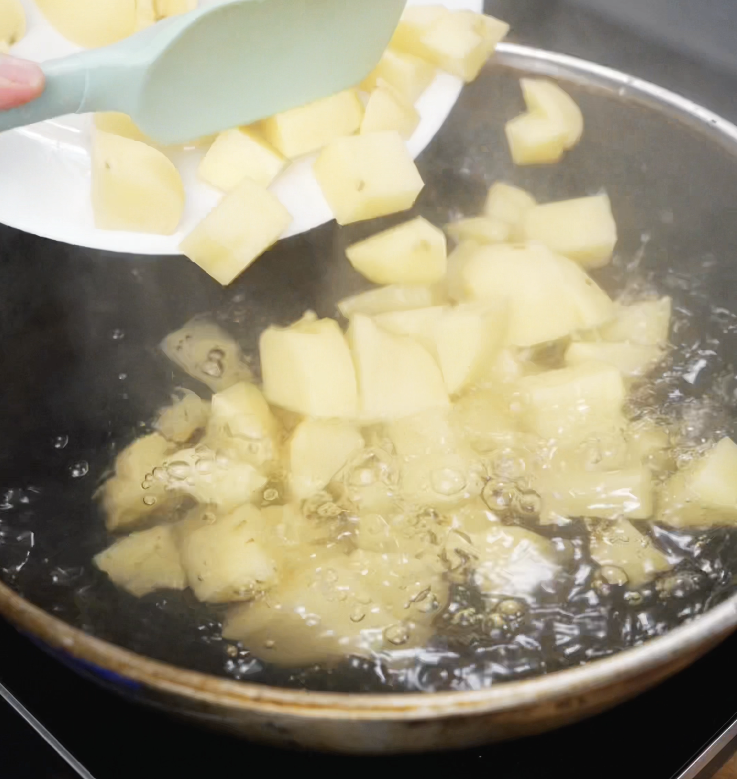 Cubed potatoes are dropped into a pot of boiling water with a spatula, beginning the process of making the mashed potato filling.