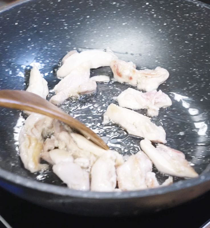 Thin strips of marinated chicken are being sautéed in a hot nonstick pan until lightly browned.
