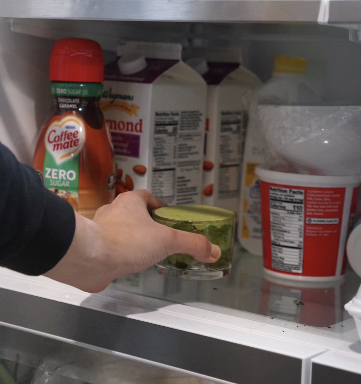 A hand places a finished matcha tiramisu cup in the refrigerator to chill and set for at least 4 hours.