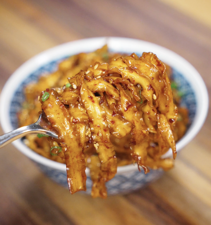 A chopstick lift of saucy noodles, showing the glistening strands coated in chili garlic butter.