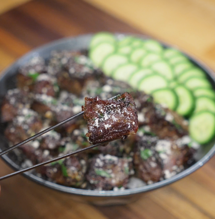 A single garlic steak bite held up with chopsticks, highlighting the caramelized crust and tender interior.