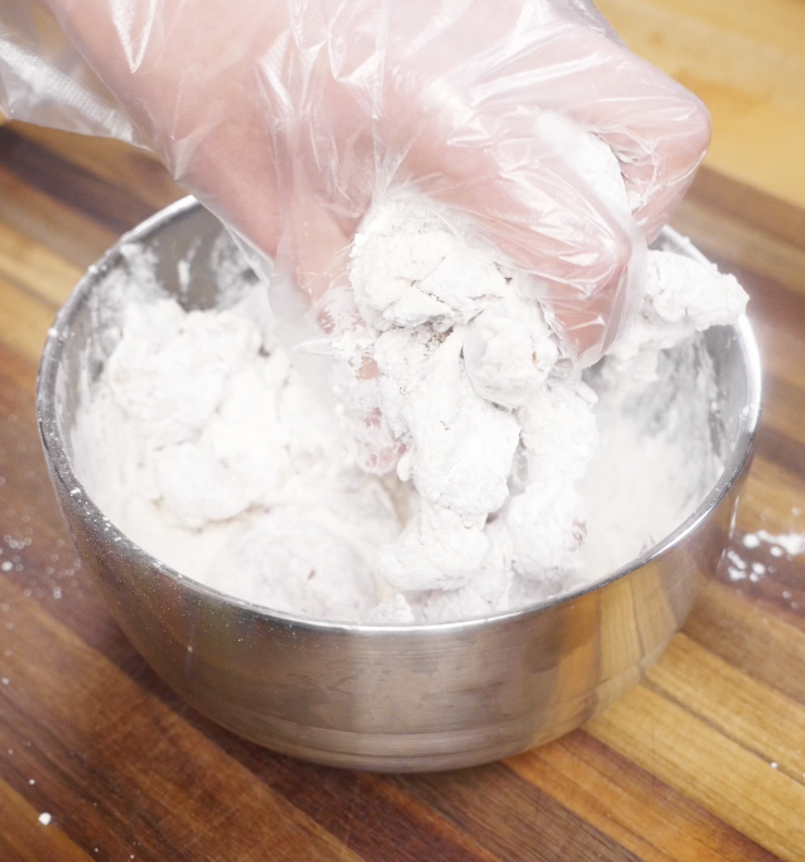 Chicken pieces being tossed in a cornstarch and flour mixture until fully coated for frying.