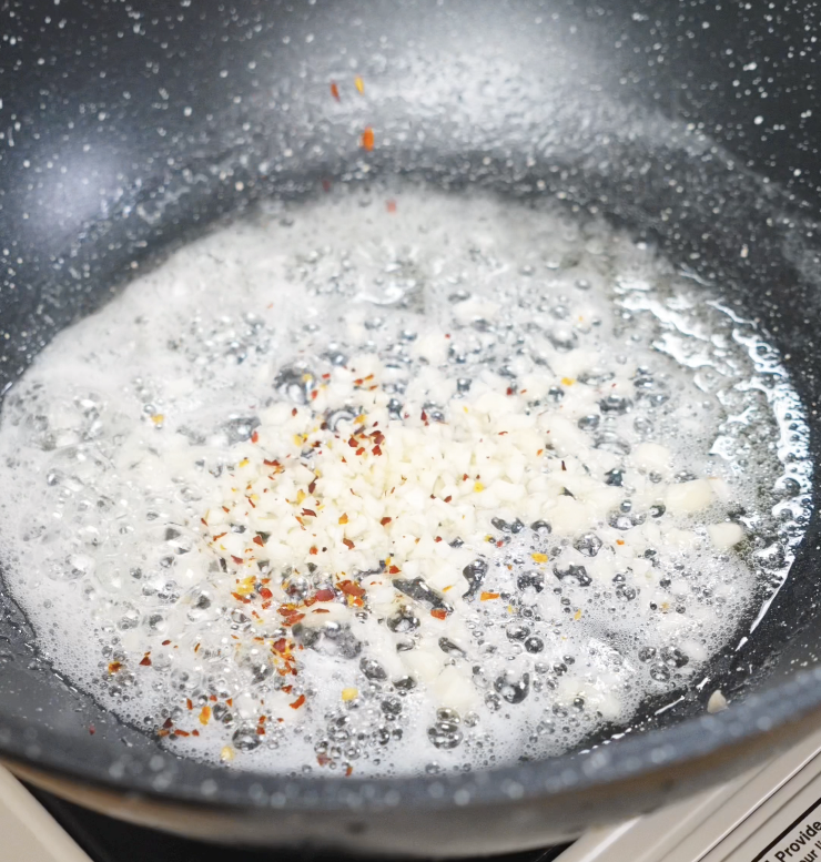 Minced garlic sizzling in melted butter with red chili flakes, releasing a fragrant aroma.