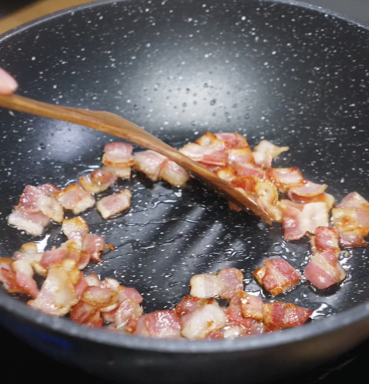 Bacon pieces are cooked in a nonstick pan until golden and crispy, releasing their flavorful fat.