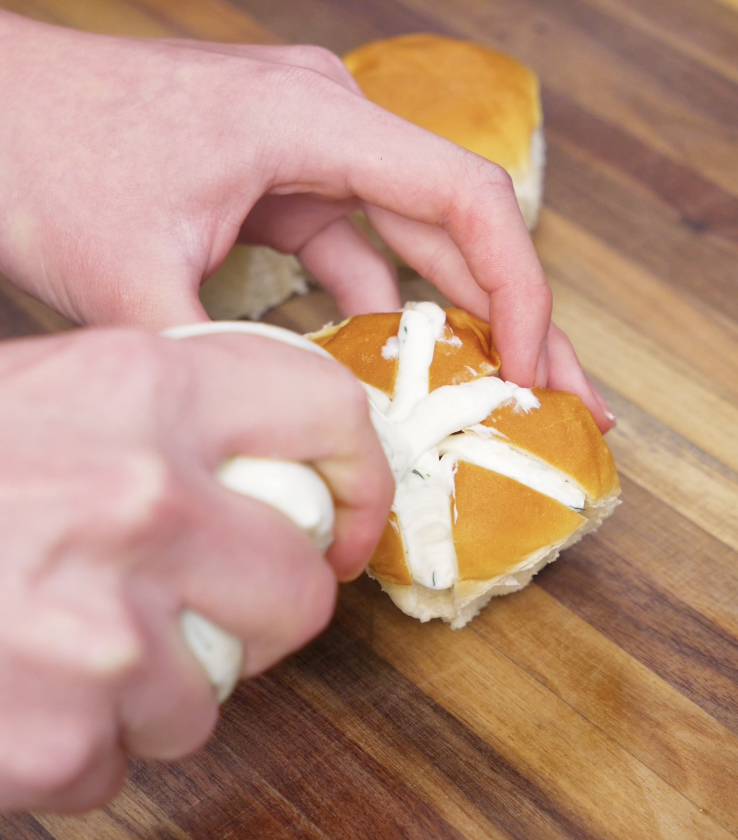 Cream cheese filling is piped into the deep slits of the bread roll using a ziploc bag, creating the signature cross pattern.