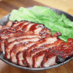 A close-up of the finished char siu pork bowl, featuring shiny red pork slices, fluffy rice, and fresh green vegetables.