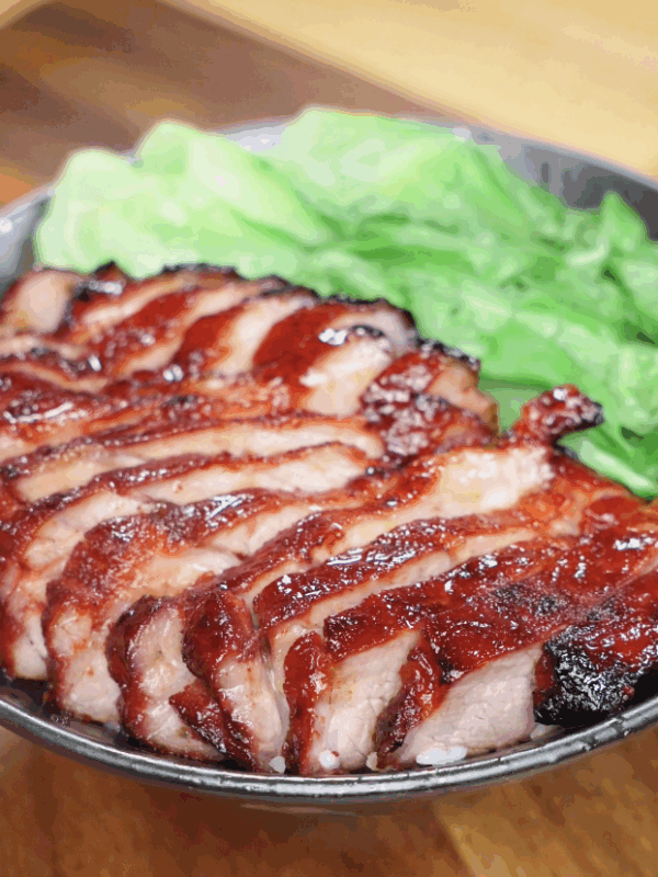 A close-up of the finished char siu pork bowl, featuring shiny red pork slices, fluffy rice, and fresh green vegetables.