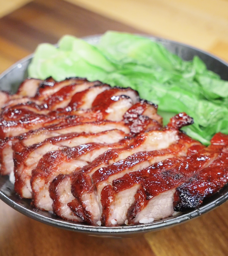 A close-up of the finished char siu pork bowl, featuring shiny red pork slices, fluffy rice, and fresh green vegetables.