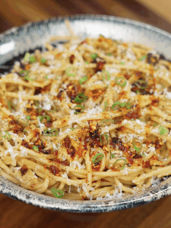 A finished bowl of miso butter pasta garnished with scallions, chili crunch, and parmesan, highlighting its rich umami flavor and glossy texture.