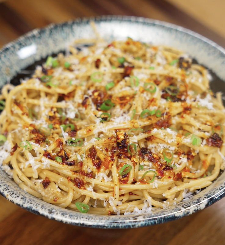 A finished bowl of miso butter pasta garnished with scallions, chili crunch, and parmesan, highlighting its rich umami flavor and glossy texture.