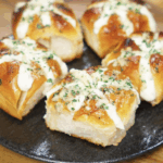 A plate of five freshly baked Korean Garlic Cheese Bread rolls, filled with cream cheese and topped with garlic butter and parsley.