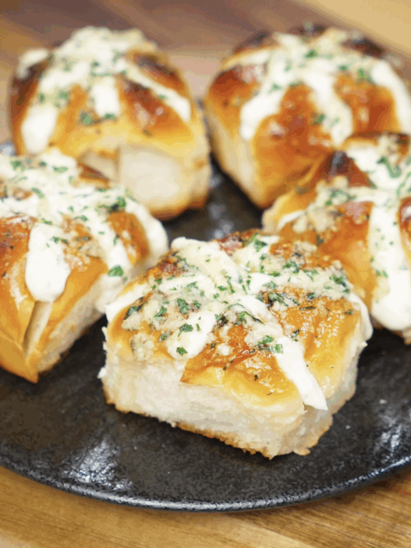 A plate of five freshly baked Korean Garlic Cheese Bread rolls, filled with cream cheese and topped with garlic butter and parsley.
