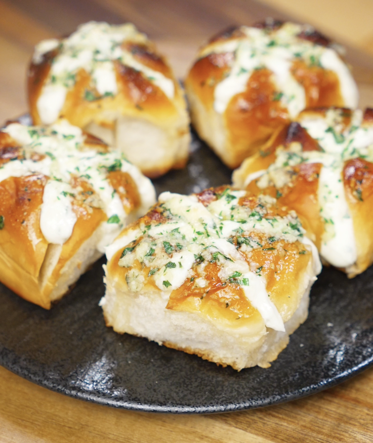 A plate of five freshly baked Korean Garlic Cheese Bread rolls, filled with cream cheese and topped with garlic butter and parsley.