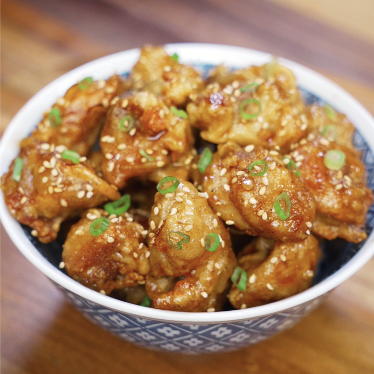 A bowl filled with golden, crispy honey butter chicken garnished with sesame seeds and scallions, ready to serve.