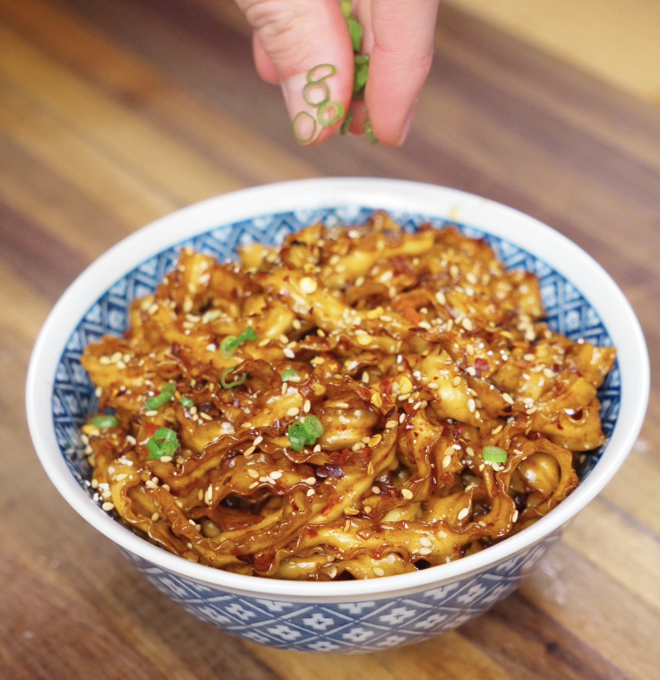A neatly twirled bowl of noodles with garlic chili oil, scallions, and sesame seeds, ready to eat.