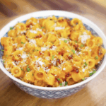 A bowl of creamy chili oil vodka pasta topped with parmesan, chives, and red pepper flakes, served in a blue patterned bowl.