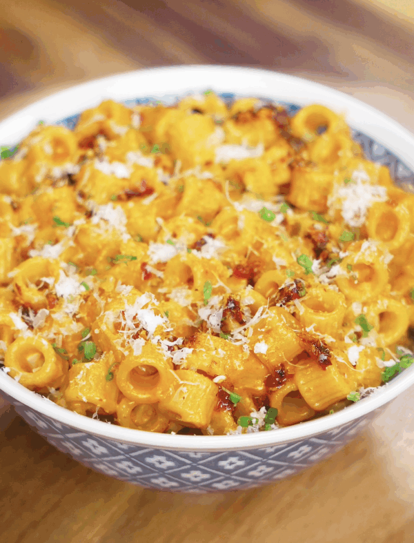 A bowl of creamy chili oil vodka pasta topped with parmesan, chives, and red pepper flakes, served in a blue patterned bowl.