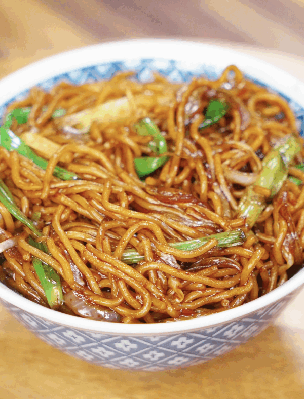 A bowl of chow mein with glossy noodles, stir-fried onions, scallions, and cabbage, ready to eat.