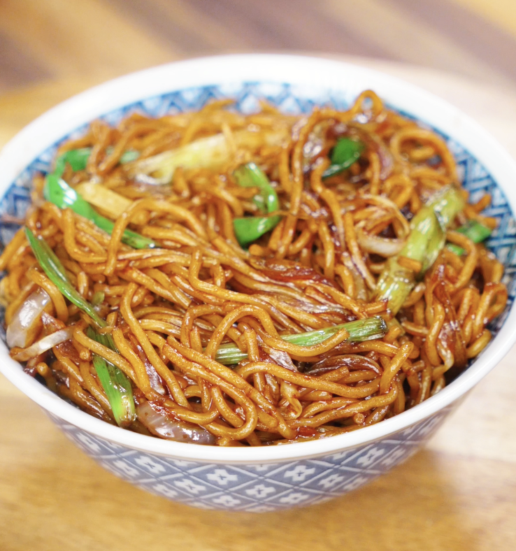A bowl of chow mein with glossy noodles, stir-fried onions, scallions, and cabbage, ready to eat.