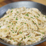 A bowl of creamy garlic fettuccini Alfredo is topped with freshly cracked black pepper and finely chopped chives for a rich, aromatic finish.