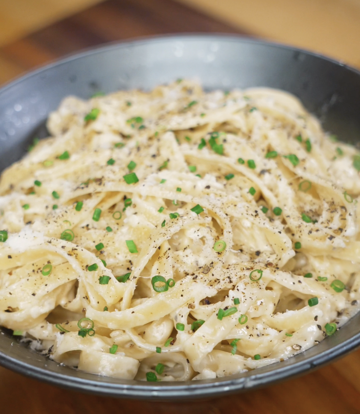 A bowl of creamy garlic fettuccini Alfredo is topped with freshly cracked black pepper and finely chopped chives for a rich, aromatic finish.