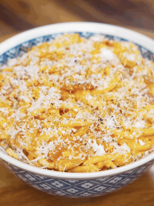 A bowl of creamy gochujang bacon noodles topped with grated parmesan, cracked black pepper, and a rich orange sauce.