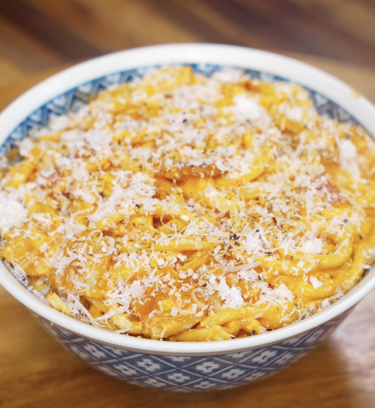 A bowl of creamy gochujang bacon noodles topped with grated parmesan, cracked black pepper, and a rich orange sauce.