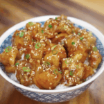 The sticky glazed Korean fried chicken is served over rice and topped with sesame seeds and scallions.