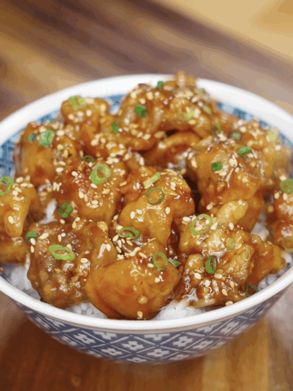 The sticky glazed Korean fried chicken is served over rice and topped with sesame seeds and scallions.