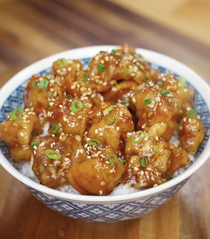 The sticky glazed Korean fried chicken is served over rice and topped with sesame seeds and scallions.