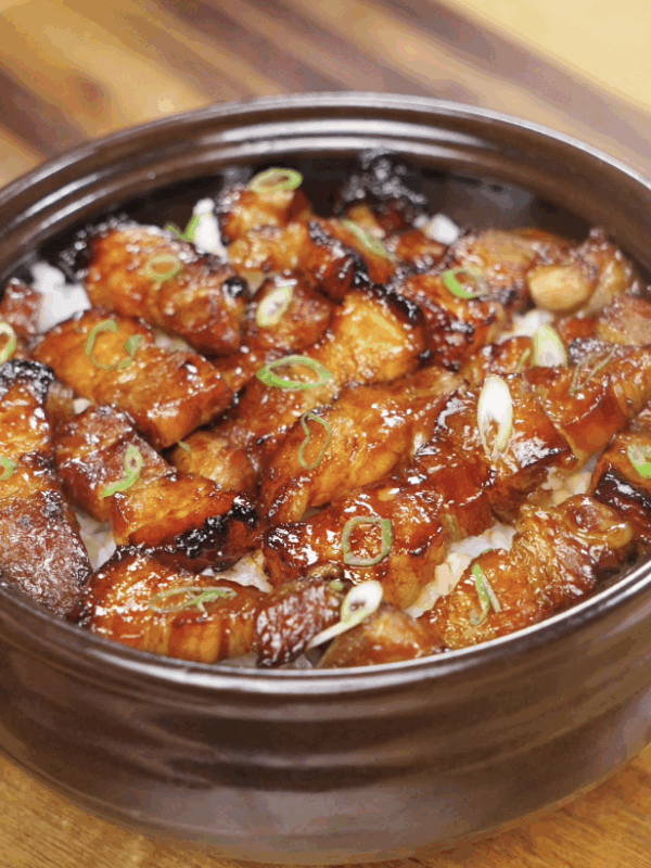 A bowl of sticky sweet pork belly bites glazed in a glossy honey-soy sauce, served over steamed rice and topped with sliced scallions.