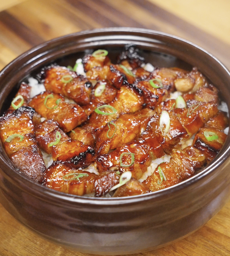 A bowl of sticky sweet pork belly bites glazed in a glossy honey-soy sauce, served over steamed rice and topped with sliced scallions.