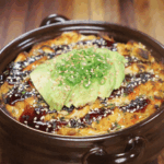 The golden-baked sushi casserole is topped with avocado slices, scallions, and sesame seeds, ready to serve.