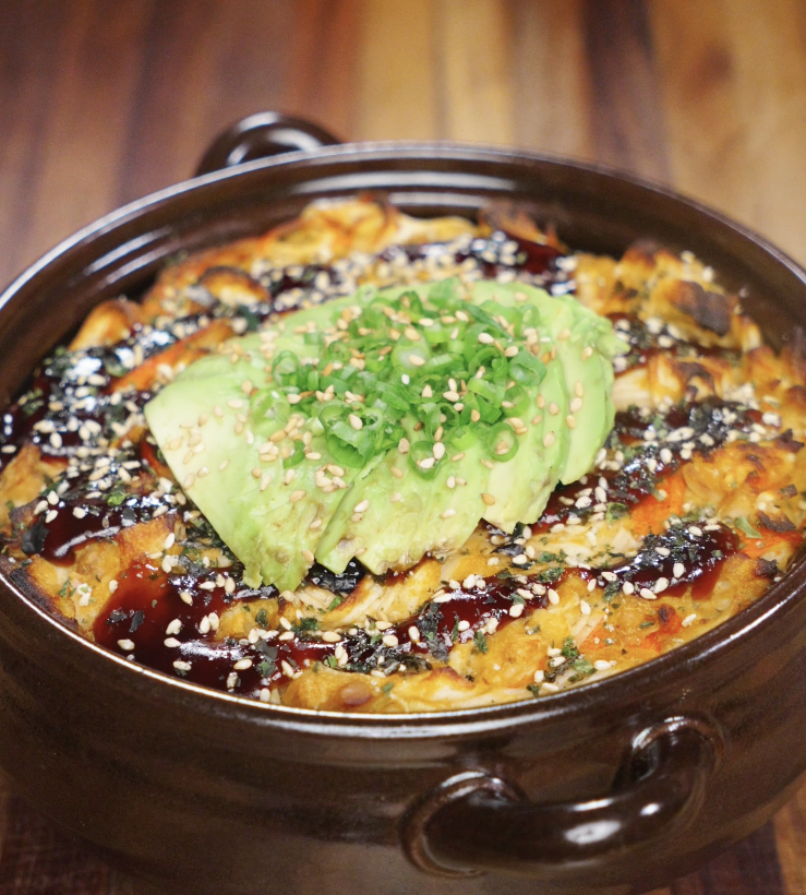 The golden-baked sushi casserole is topped with avocado slices, scallions, and sesame seeds, ready to serve.