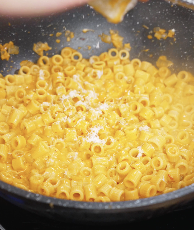Freshly grated parmesan cheese is sprinkled over the finished chili oil vodka pasta while still in the pan.