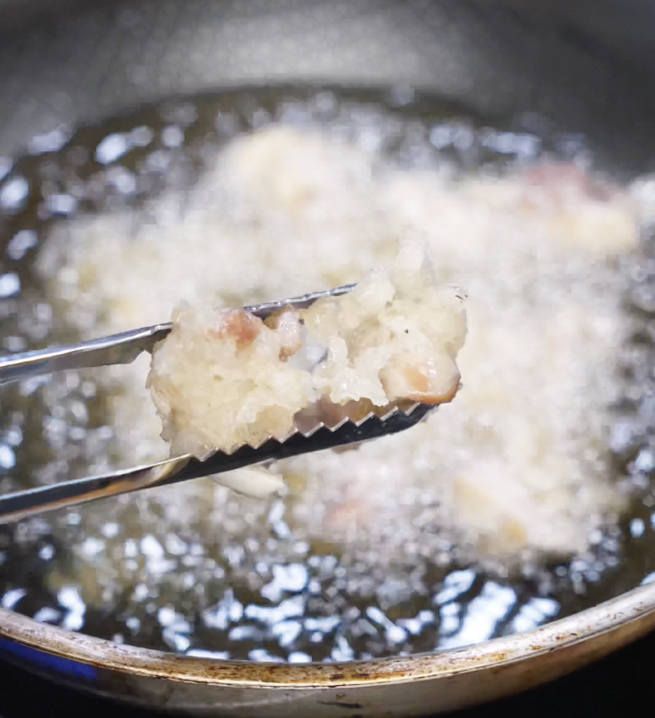 Chicken pieces frying in oil during the first fry stage, lightly golden and bubbling.
