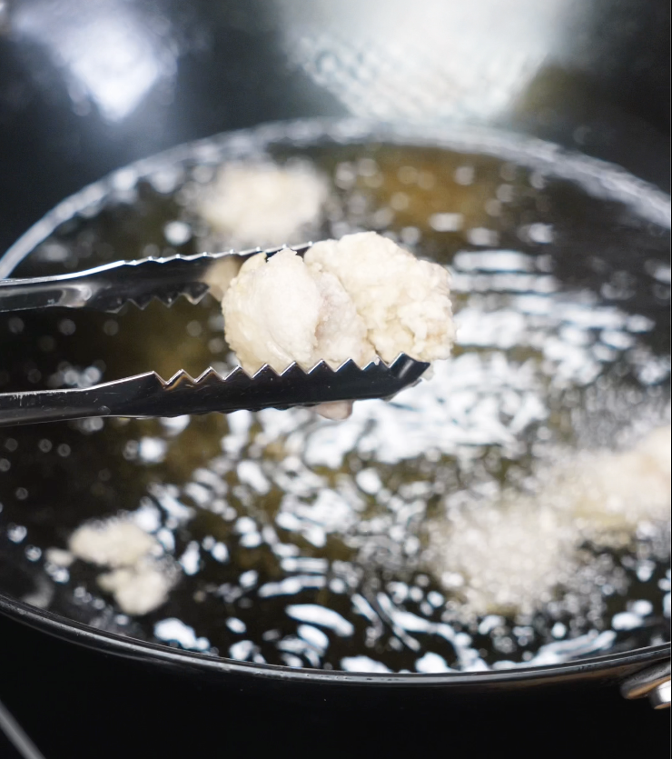 A pale, battered piece of chicken being lifted from hot oil during the first fry.