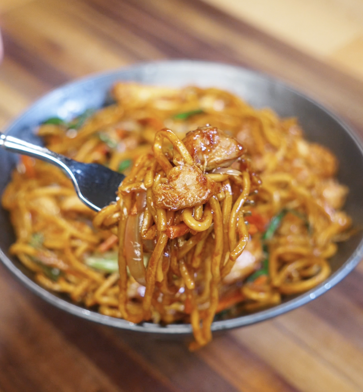 A close-up of Chicken Lo Mein twirled on a fork, showcasing saucy noodles and tender chicken pieces.