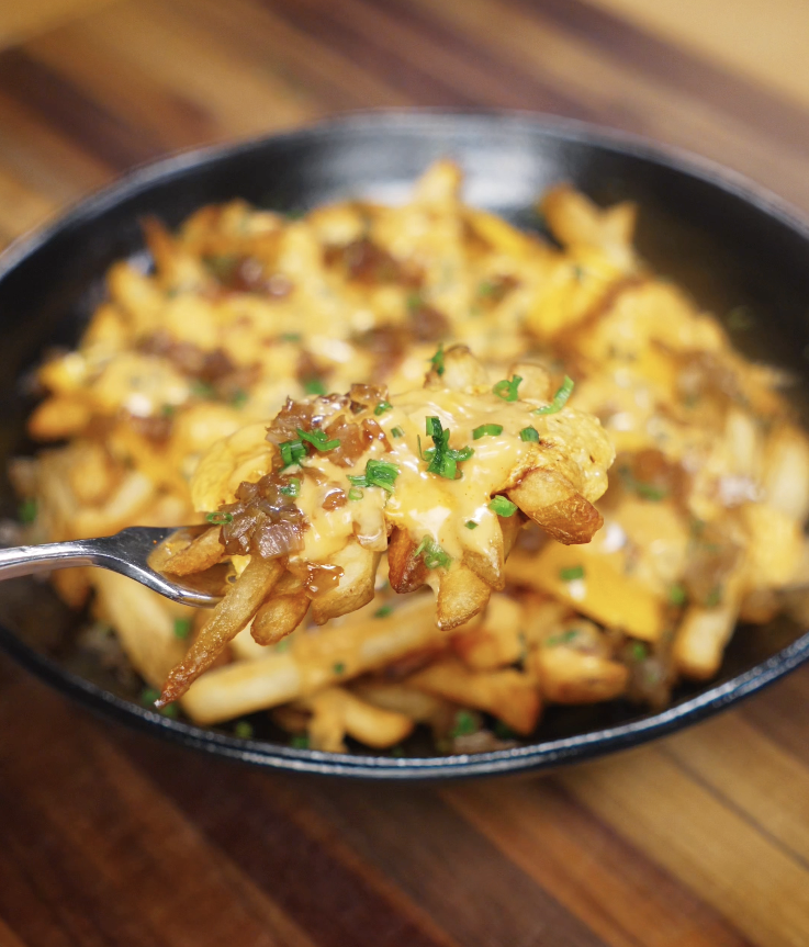 A close-up of loaded fries being lifted with a fork, dripping with melted cheese, onions, and gochujang animal sauce.