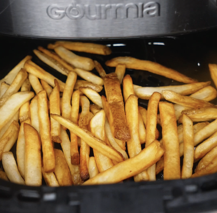 Frozen fries are cooking in the air fryer basket until crisp and golden brown.