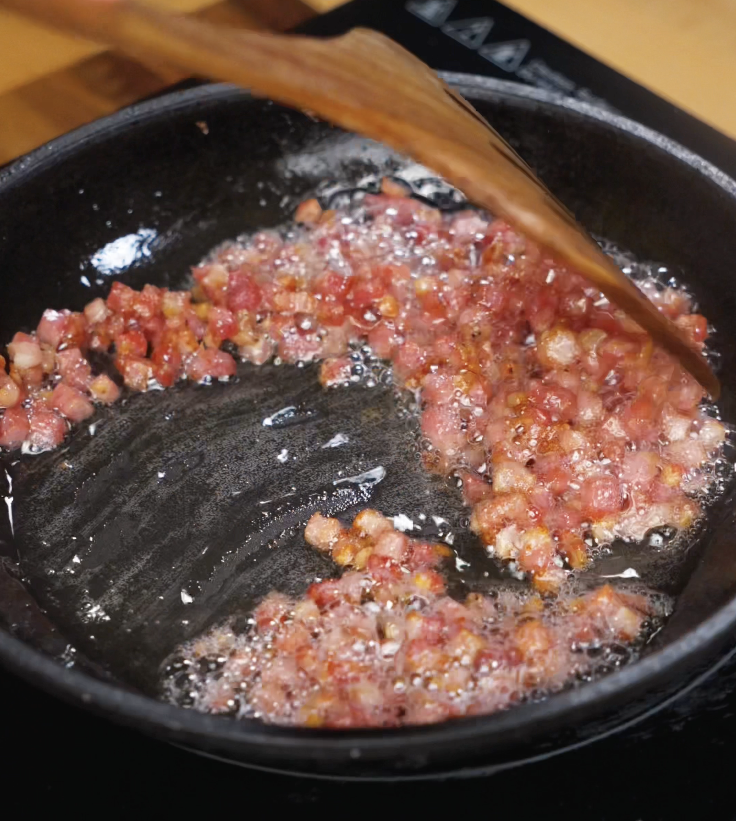 Diced pancetta is rendered in a skillet until crispy and golden, releasing its rich, savory fat.