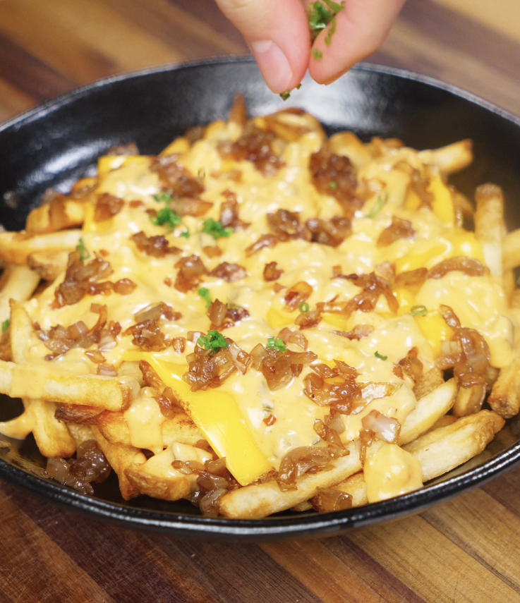 Fresh chopped chives are being added to the loaded fries for a bright, flavorful finish.