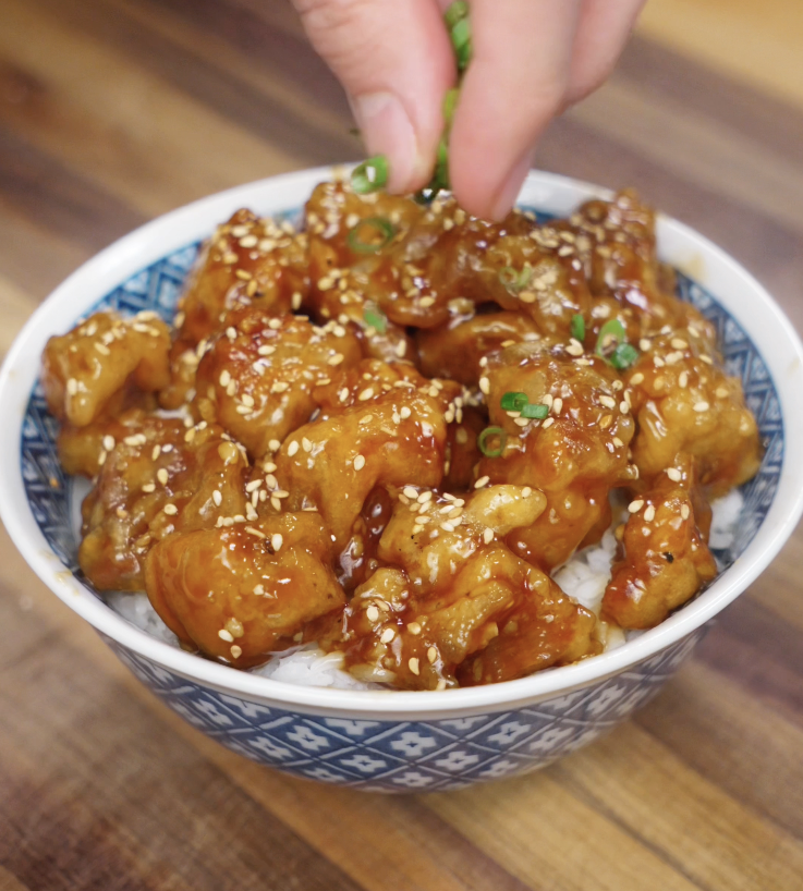 A final sprinkle of sliced scallions is added by hand to finish the Korean fried chicken rice bowl before serving.