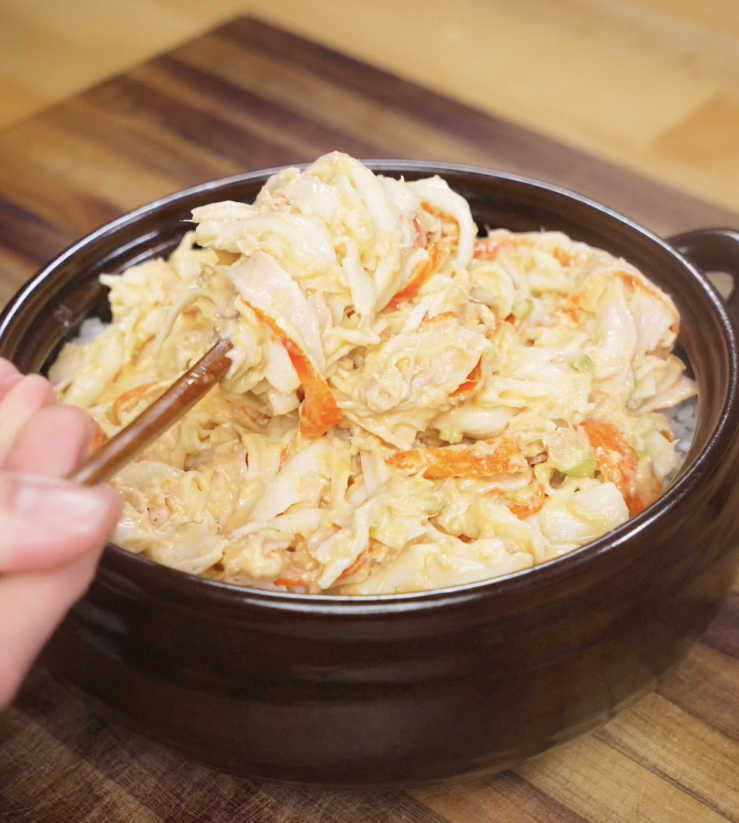 The creamy crab and tuna mixture is spread evenly over a layer of seasoned sushi rice in a dark baking dish.
