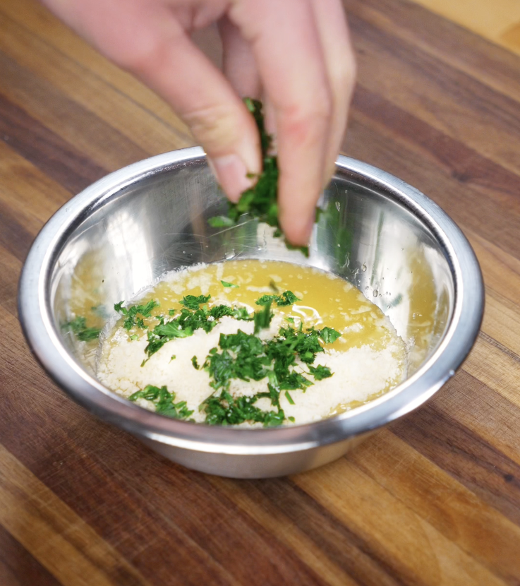 Chopped parsley is sprinkled into a bowl of melted butter and parmesan to create the garlic butter glaze.