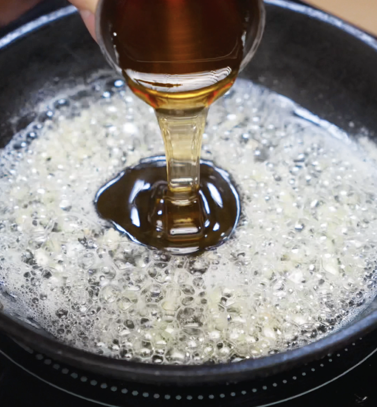 Golden honey being poured into a pan of bubbling butter and garlic, forming the base of the honey butter glaze.
