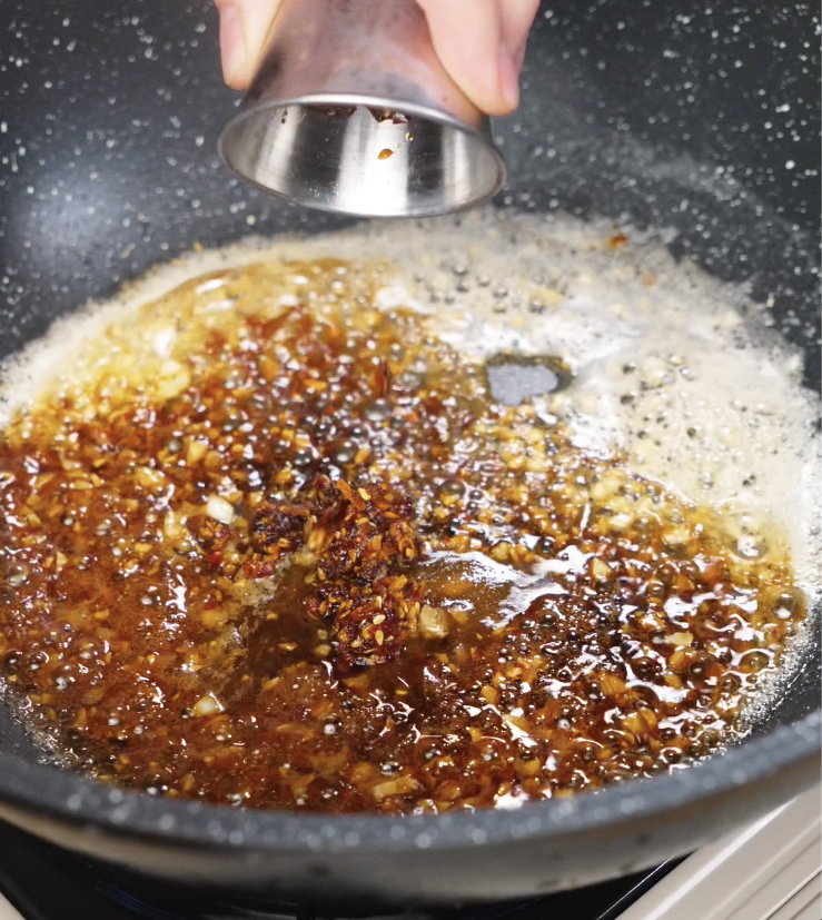 Soy sauce and chili oil being added to the pan, blending with the garlic butter to create a spicy, umami-rich base.