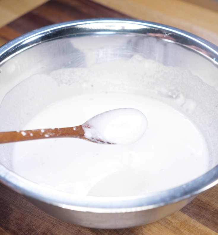 A spoon being dipped into a bowl of smooth rice flour and potato starch batter, perfectly mixed for frying.