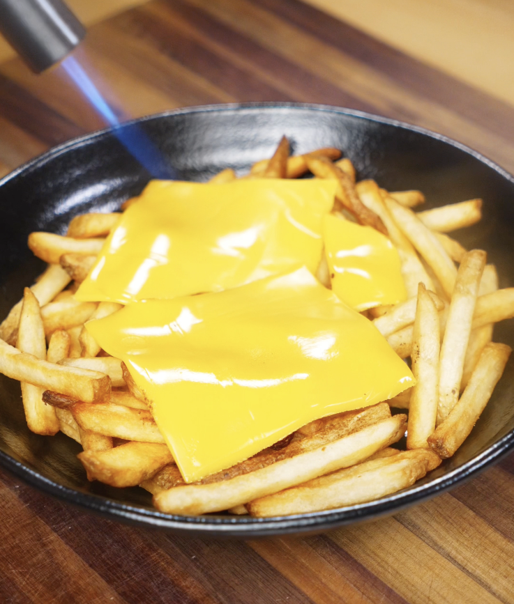 American cheese slices are being torched to melt over a hot bed of fries for the loaded fries base.